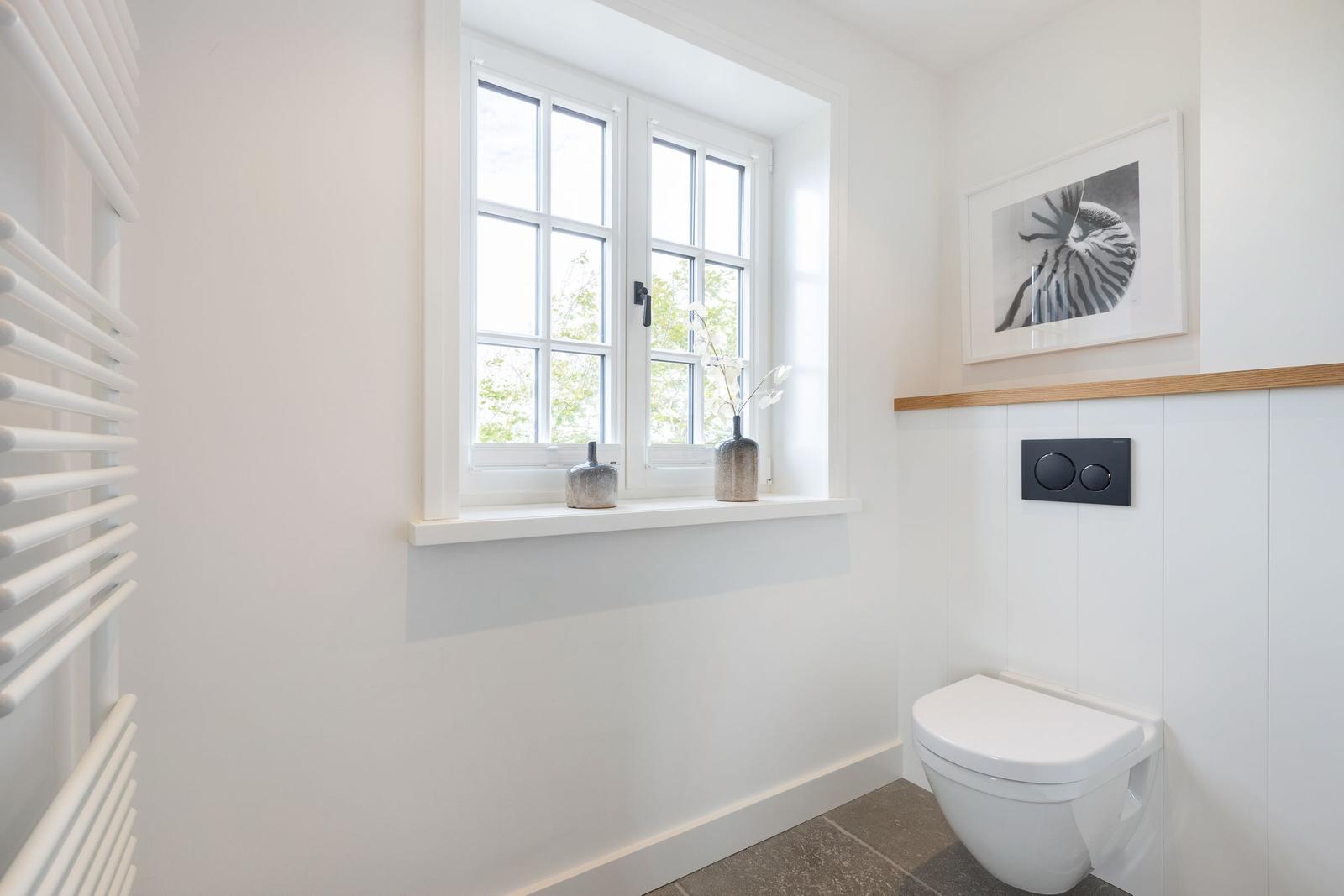 Bathroom with toilet, window, and wall art.