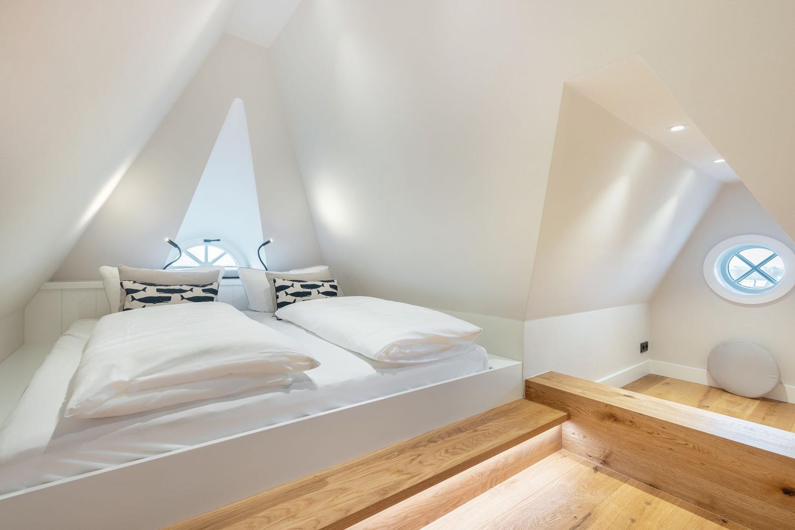 Bedroom with double bed, wooden steps, and round window.