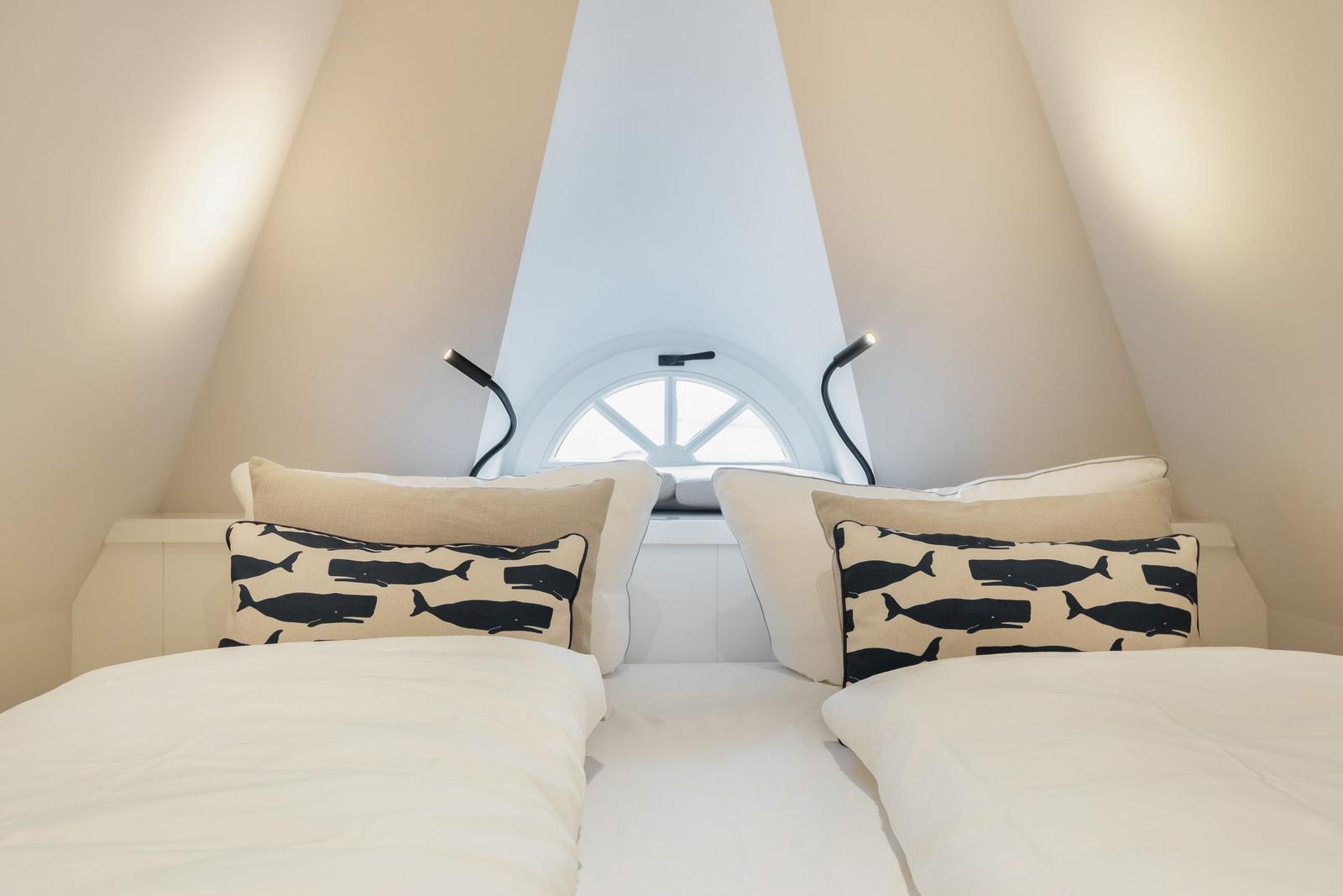 Two beds with pillows under a window in an attic room.