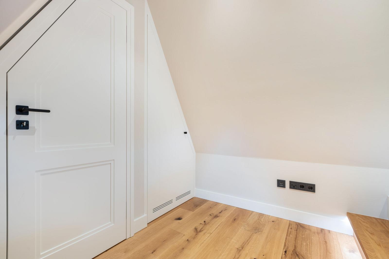 Room with wooden floor, white door, and sloped wall