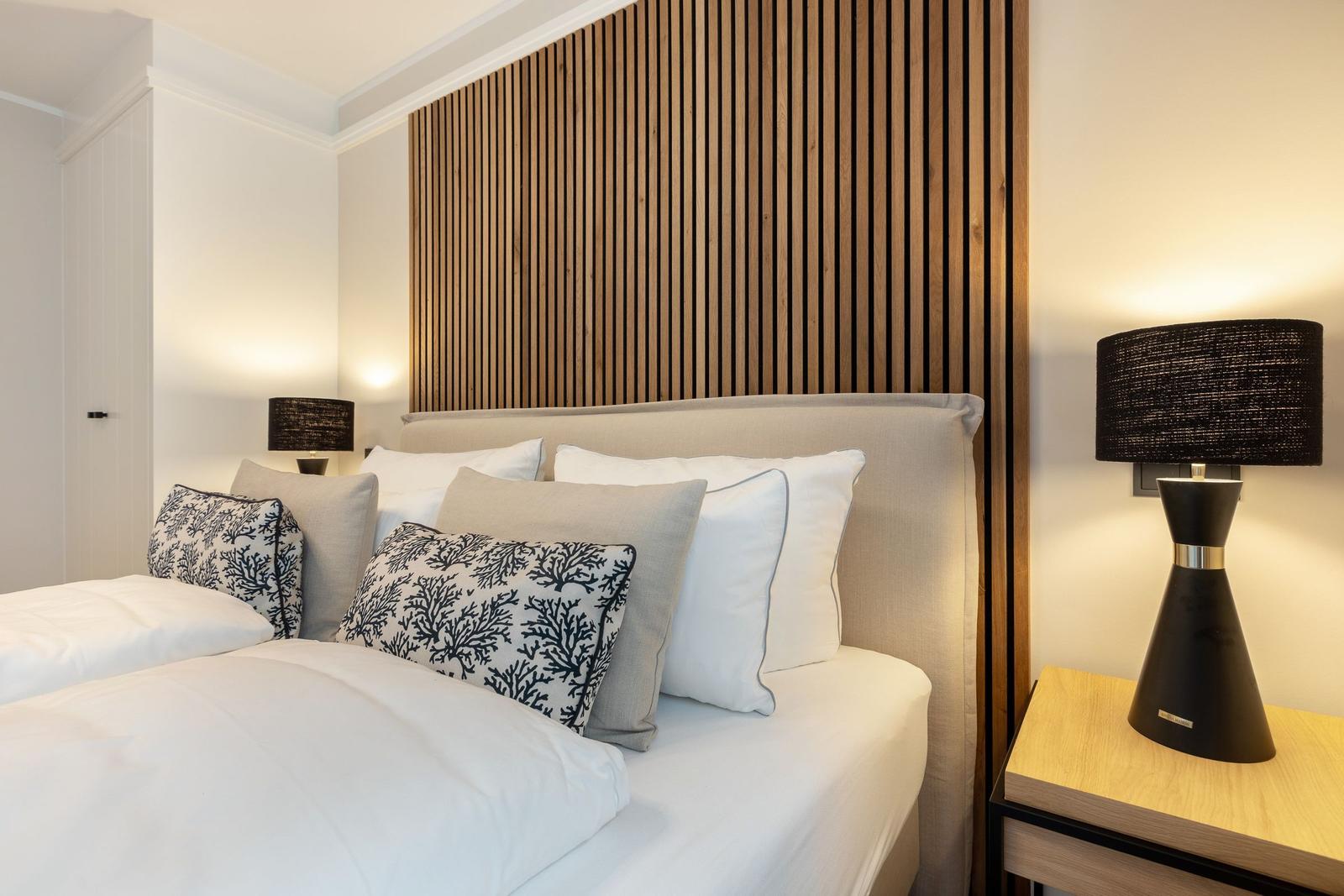 Bedroom with bed, wooden wall, and nightstand with lamp.