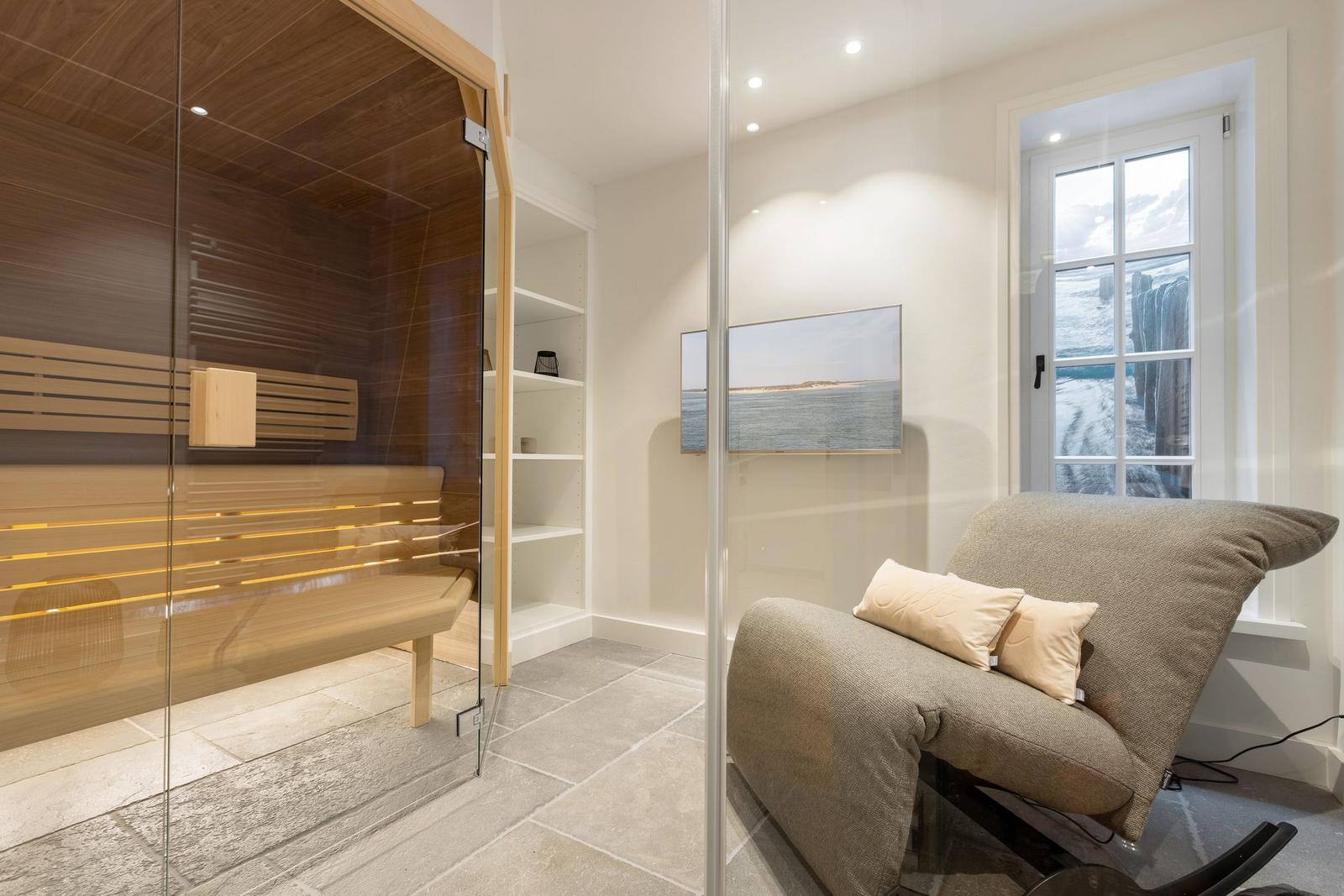 Sauna with wooden benches and glass wall. Adjacent room with chair and window.