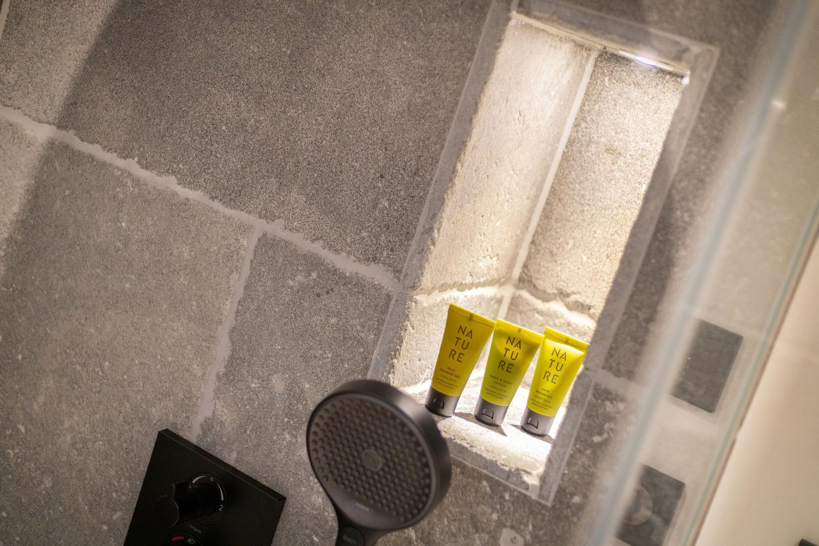 Shower cabin with shower head and three yellow care products in stone niche.