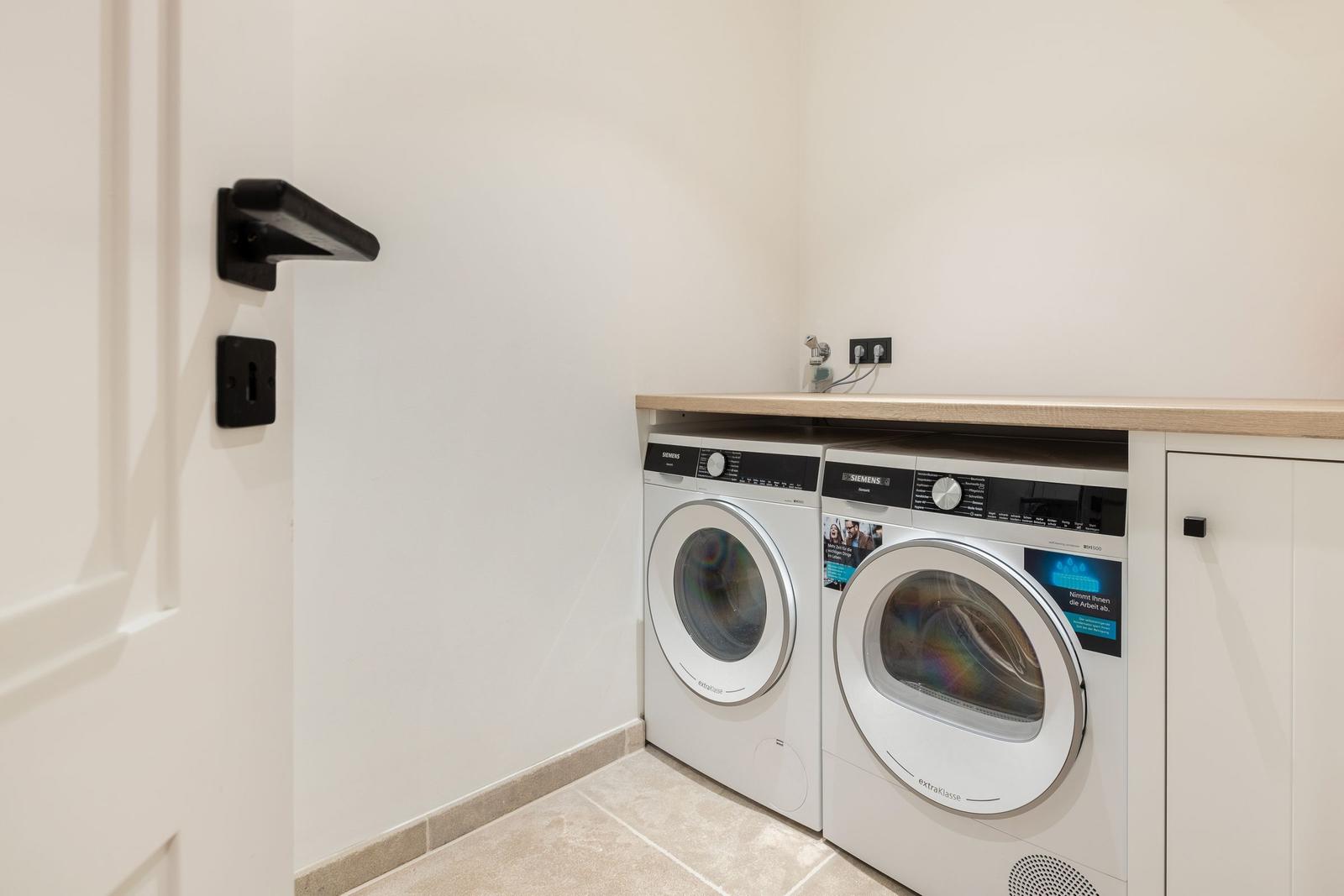 Washing machine and dryer in a room with wooden countertop and white door.