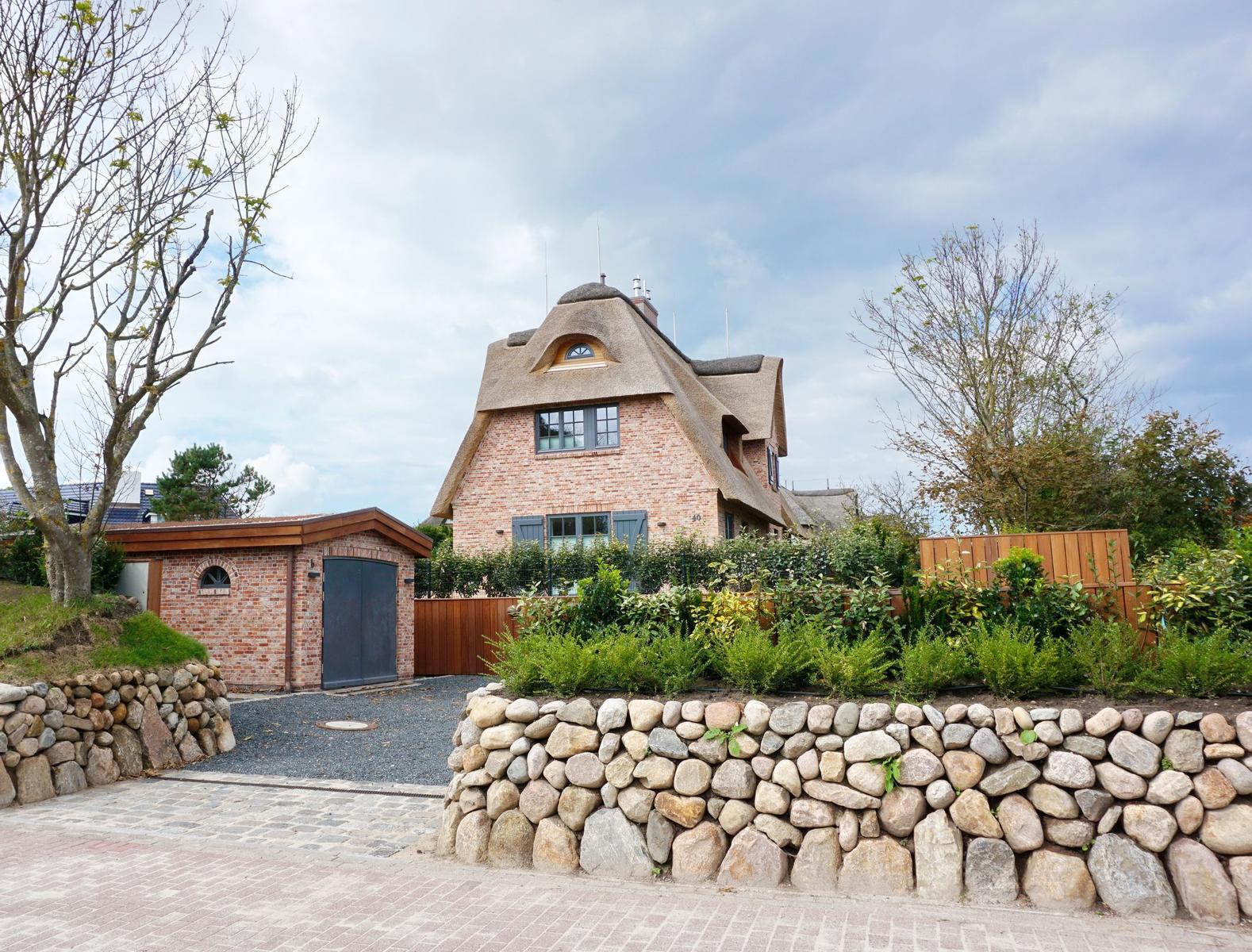 House with thatched roof, stone wall, and paved driveway
