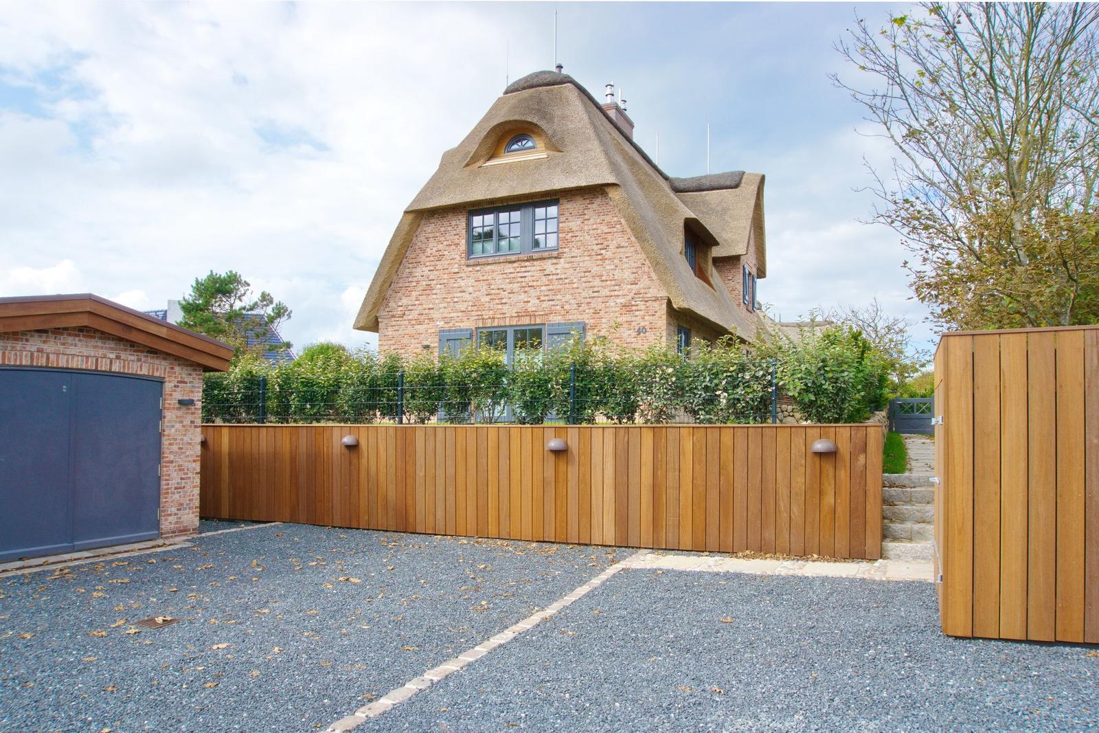 House with thatched roof, wooden fence, and gravel driveway.