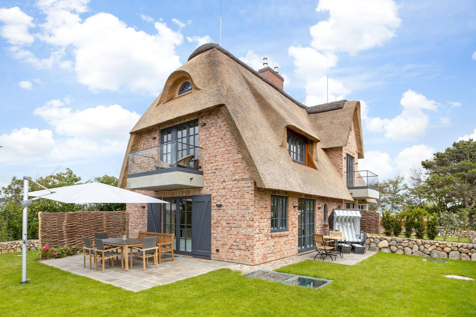 House with thatched roof and terrace with garden furniture.
