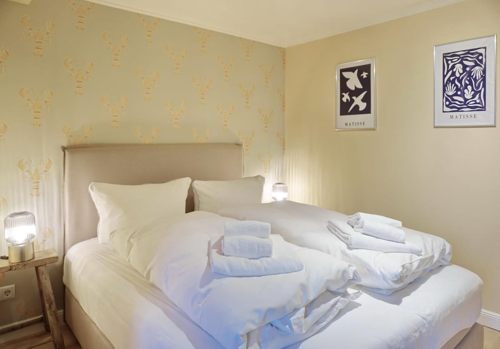 Bedroom with bed, towels, and wallpaper with lobster motifs.