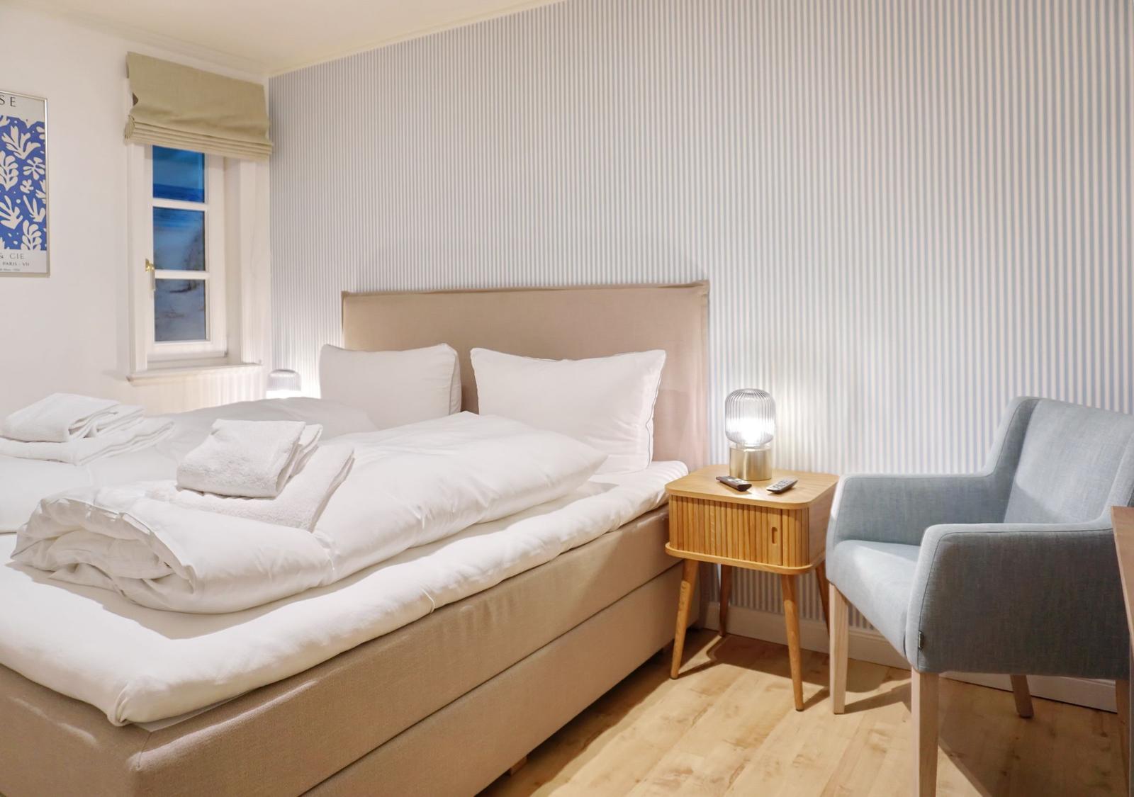 Bedroom with bed, nightstand, and chair. Wall with striped pattern.