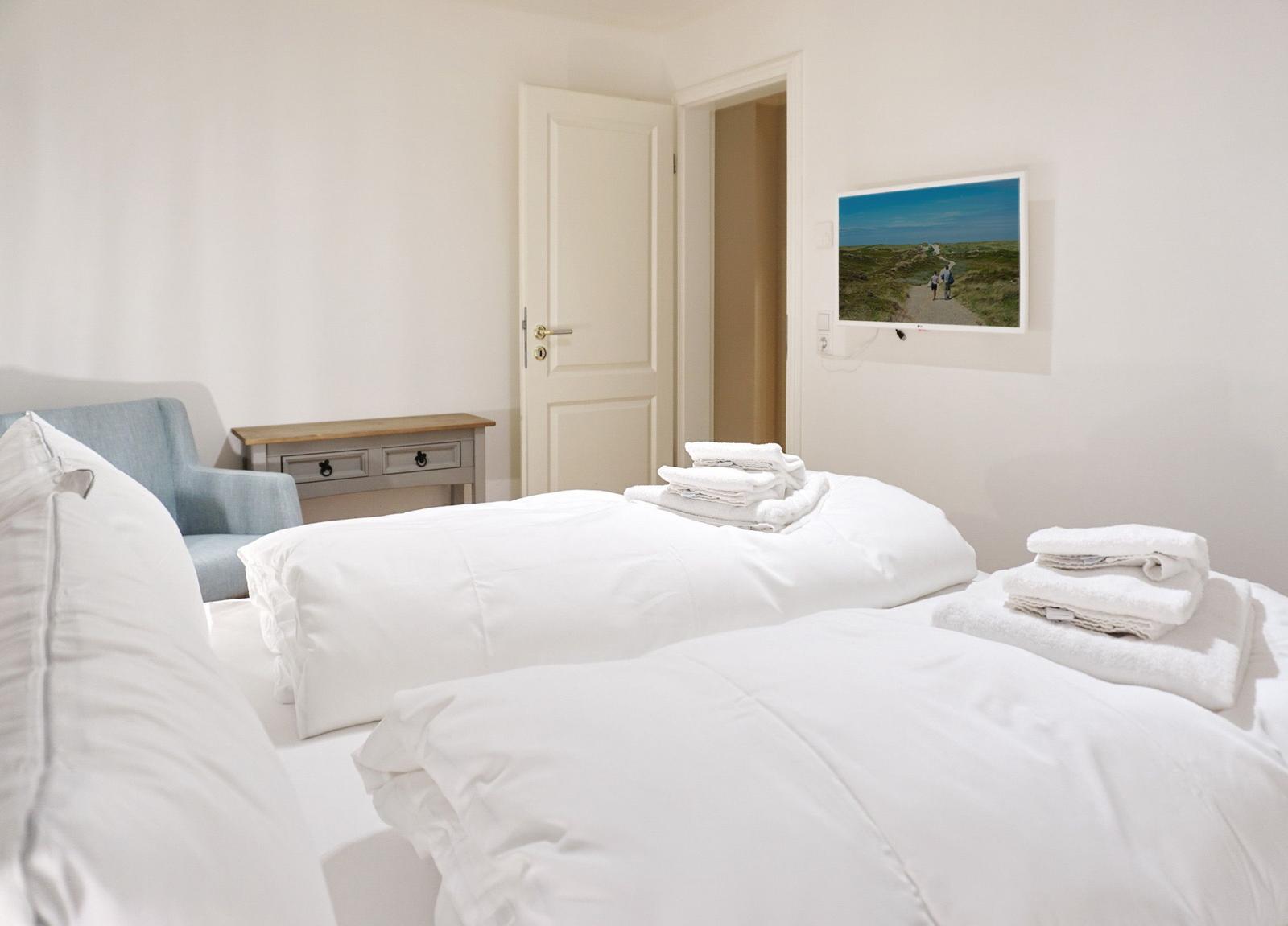 Bedroom with white bed, blue seating, and wall picture.