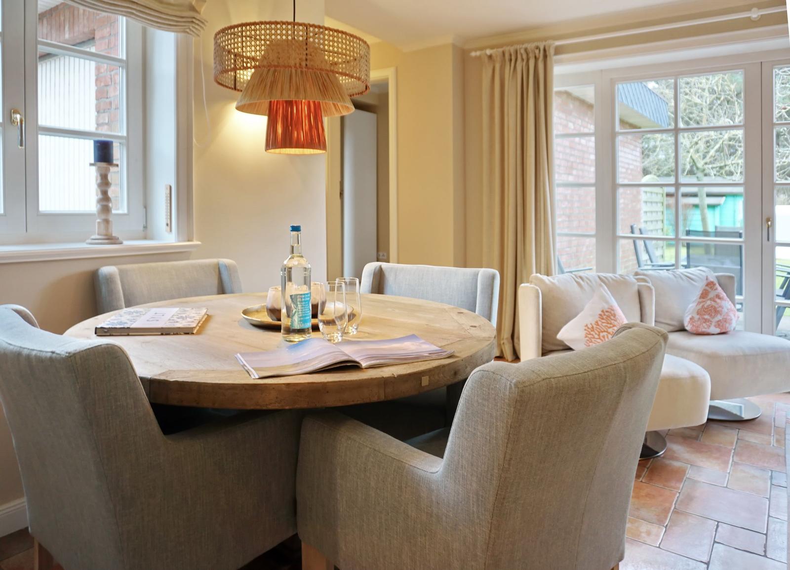 Round wooden table with chairs, seating area, and windows in dining space.