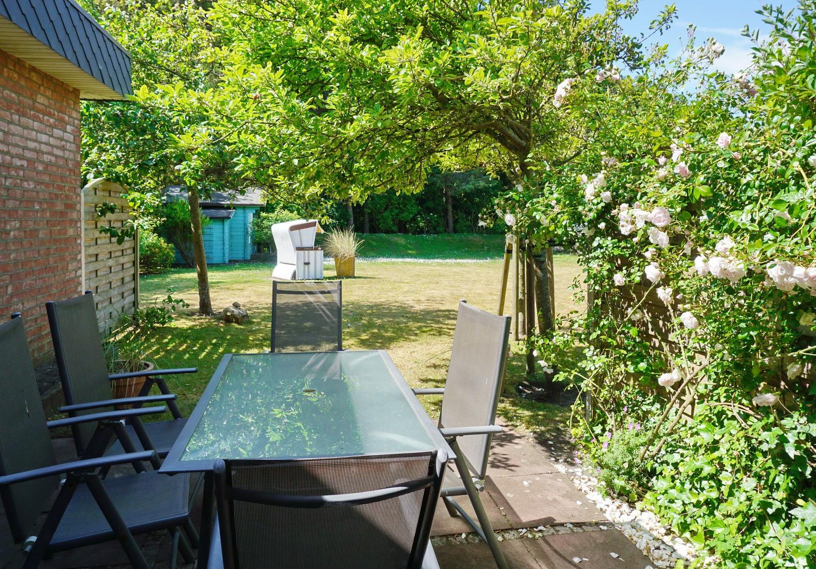 Garden with seating, flowers, and tree. Background with lawn and house.