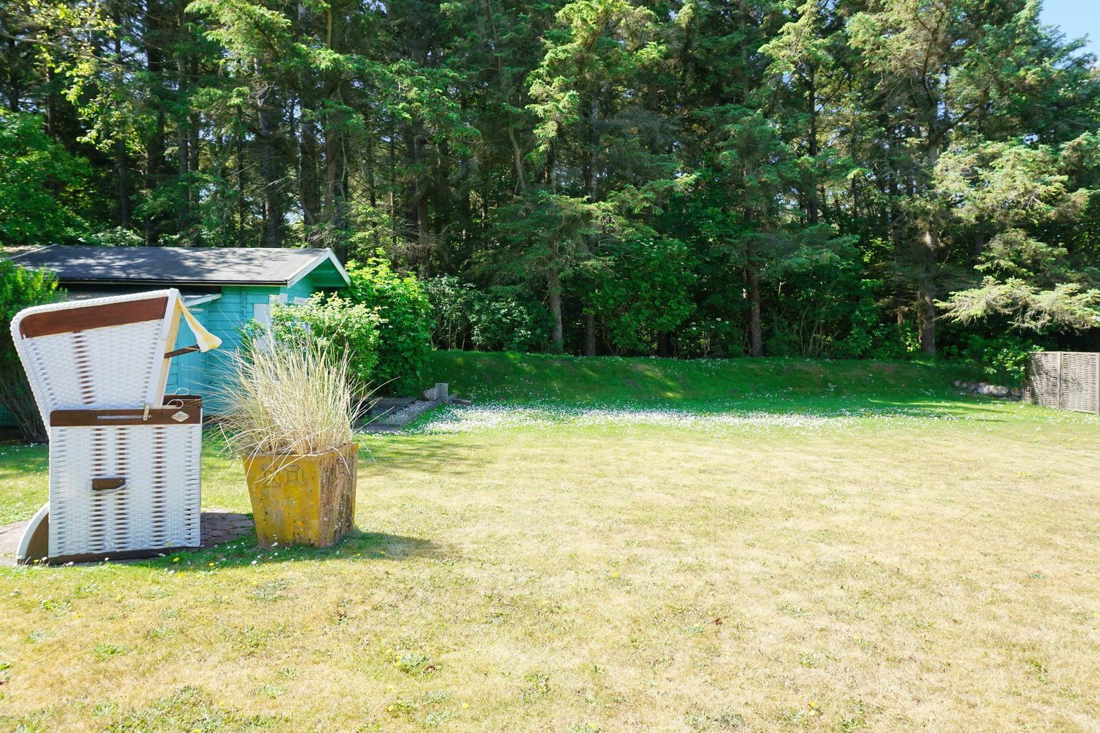 Green garden with beach chair and small house in the background.
