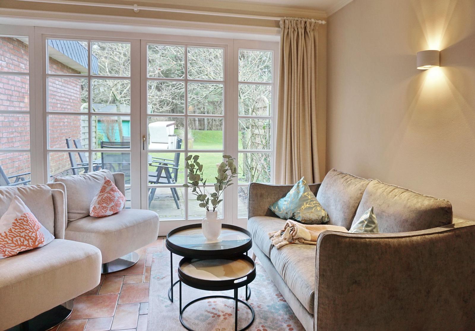 Living room with sofa, armchairs and table. French doors lead to the terrace.