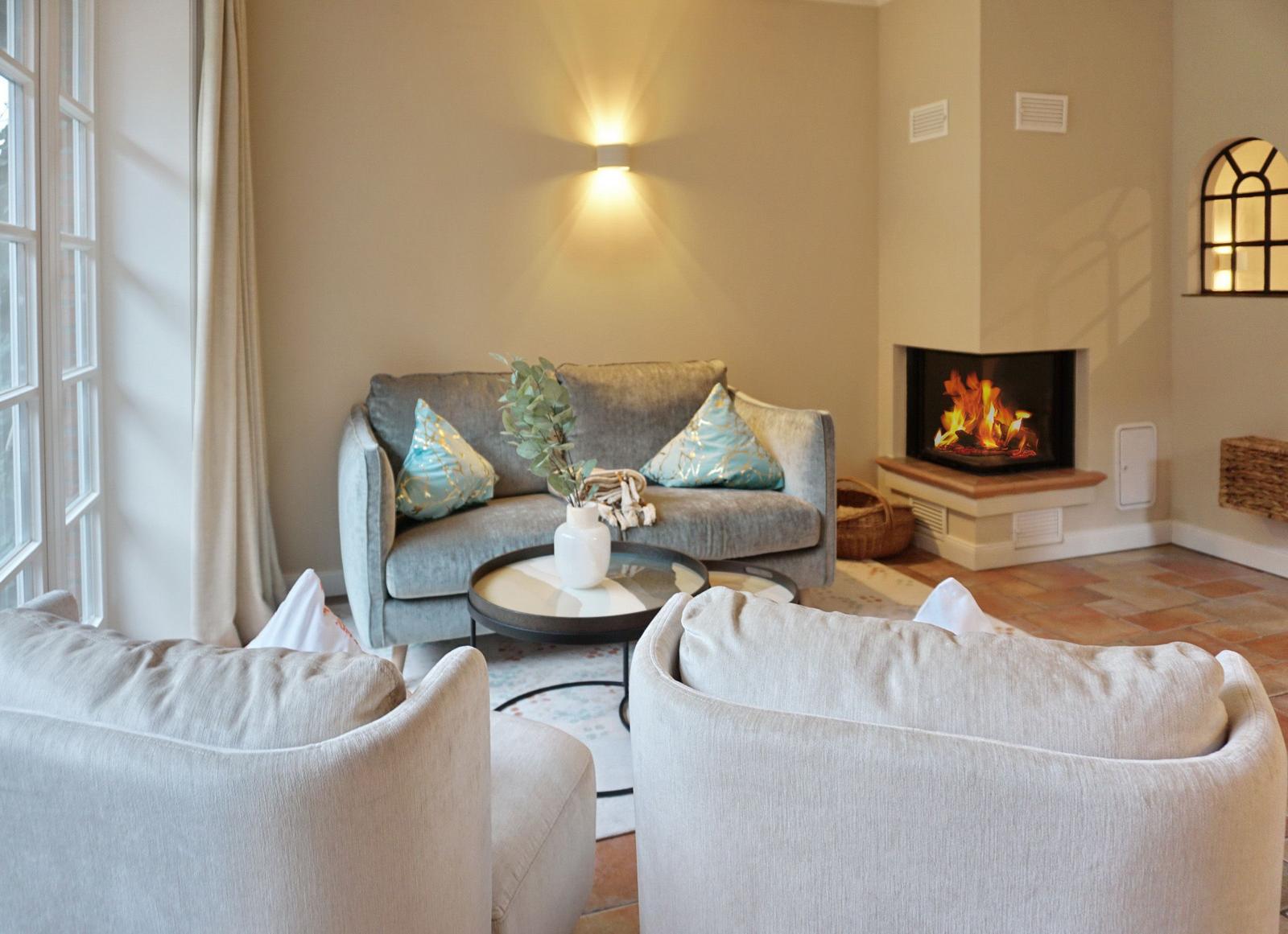 Living room with sofa, fireplace, and two armchairs. Window and wall lighting visible.