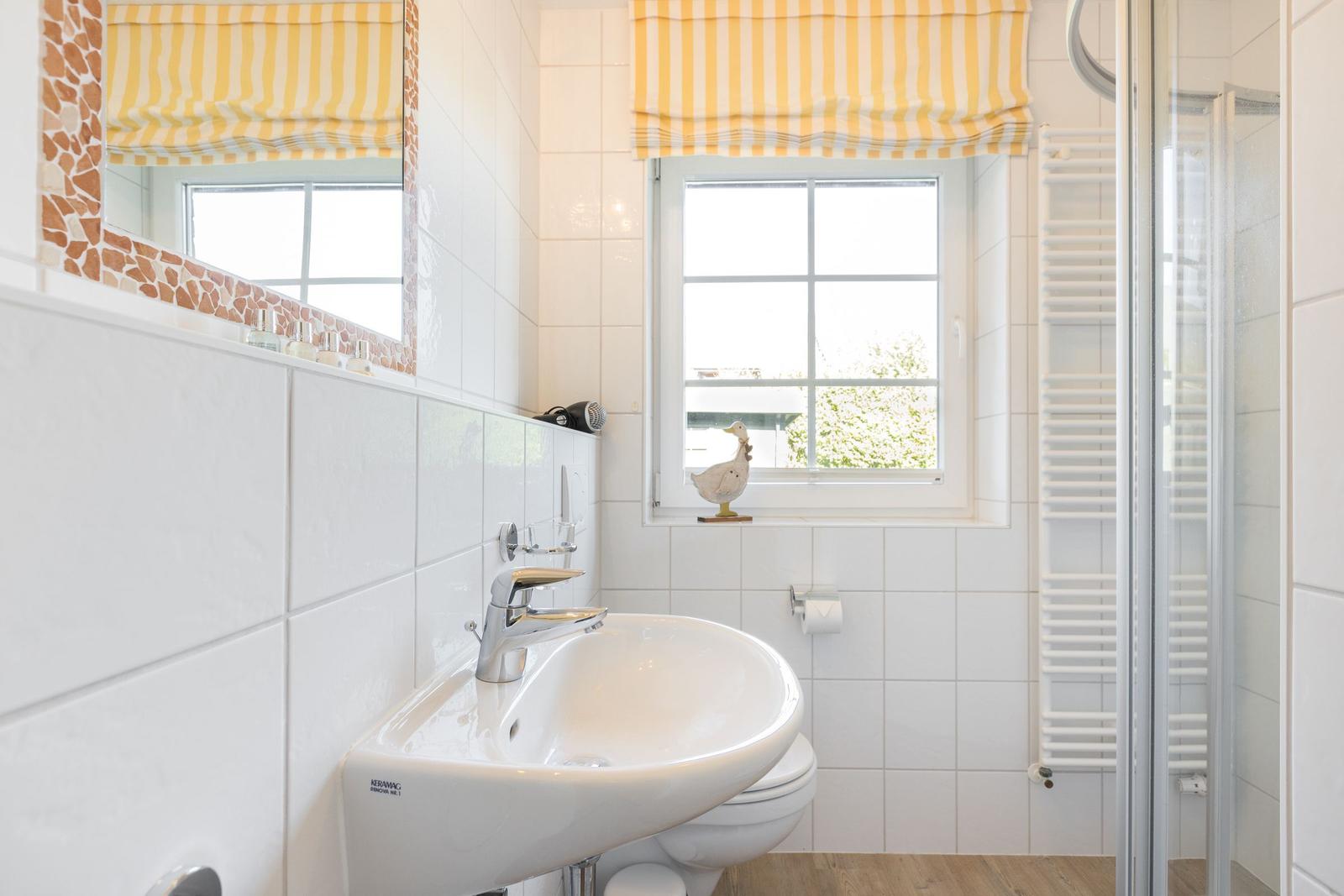 Bathroom with sink, toilet, and shower. Window with yellow-white roller blind.