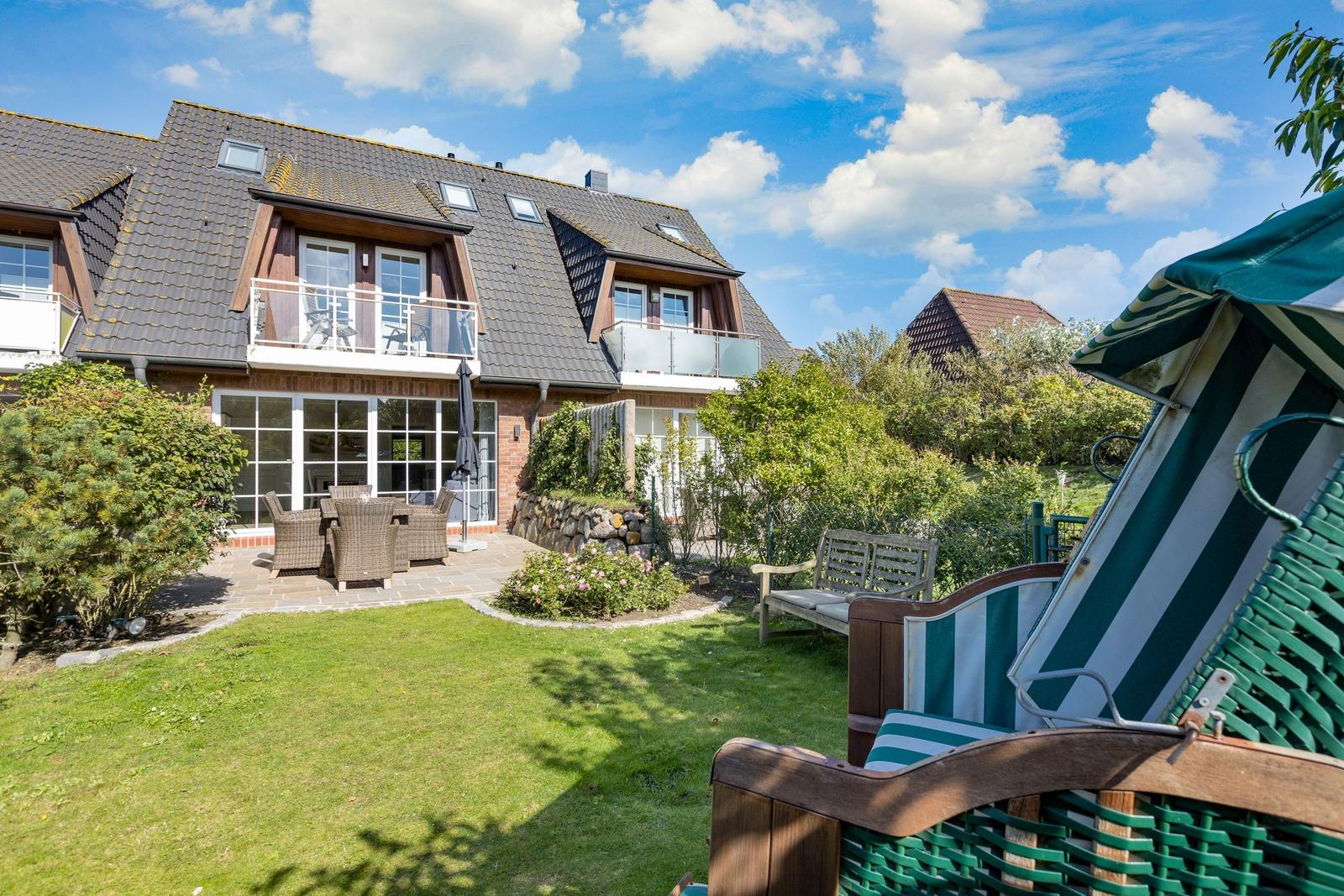 House with balcony, garden, and beach chairs under blue sky.