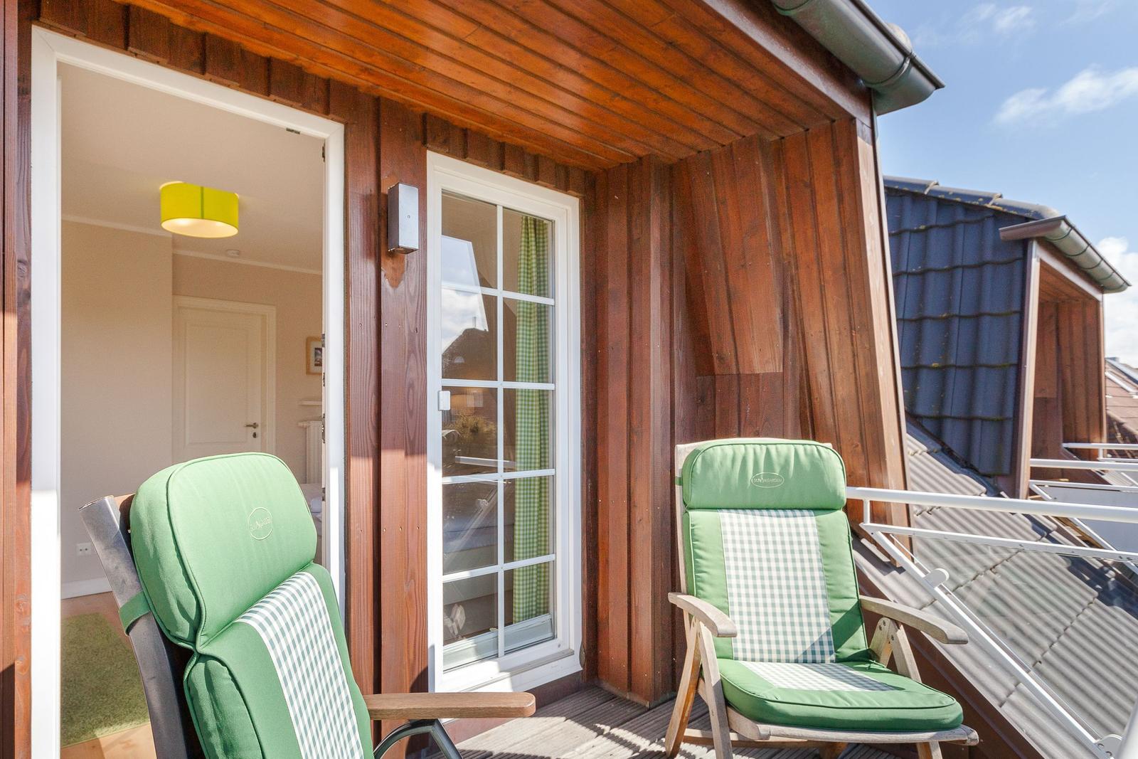 Terrace with two green chairs in front of wooden house with glass door.