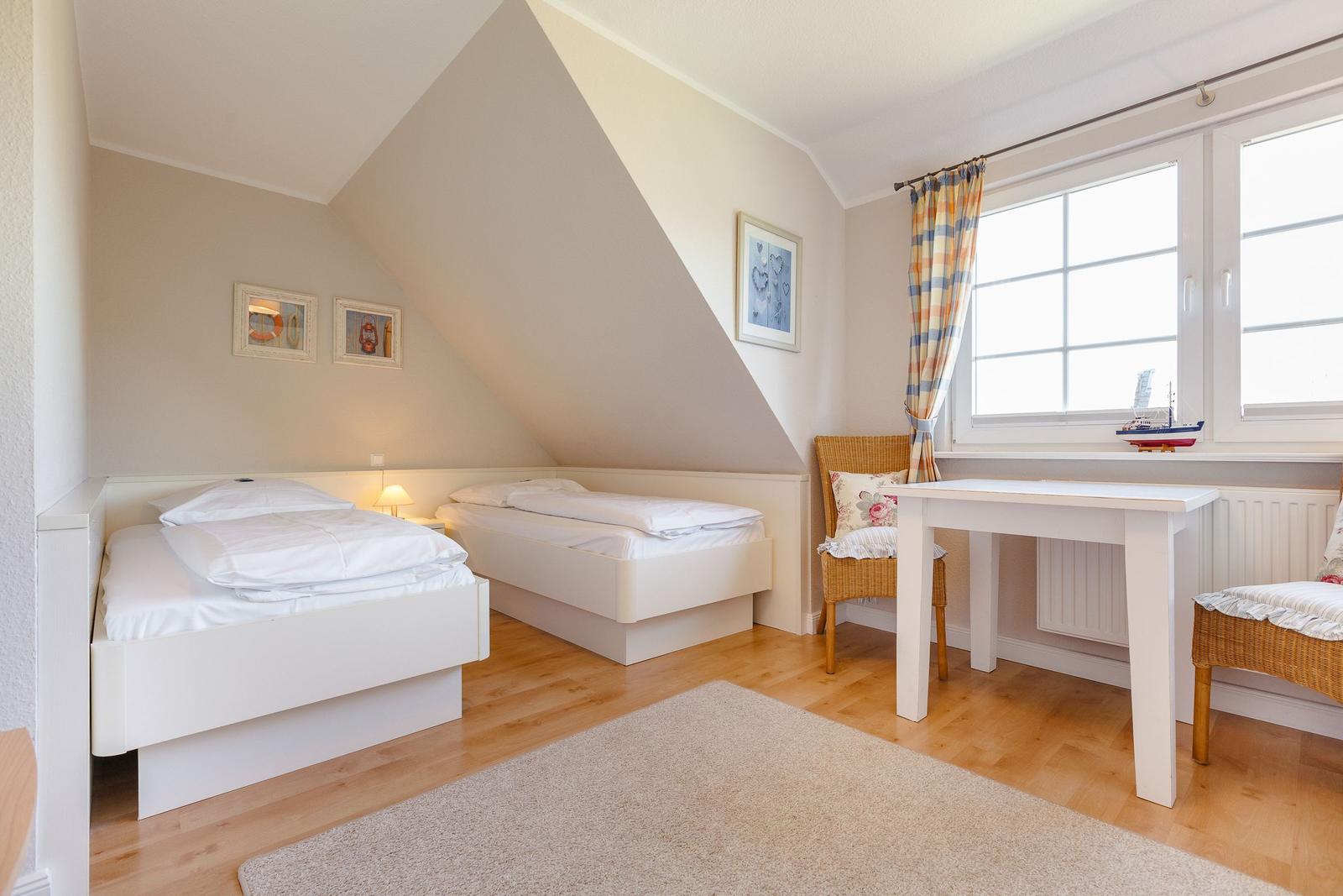 Room with two beds, desk and window with curtain.