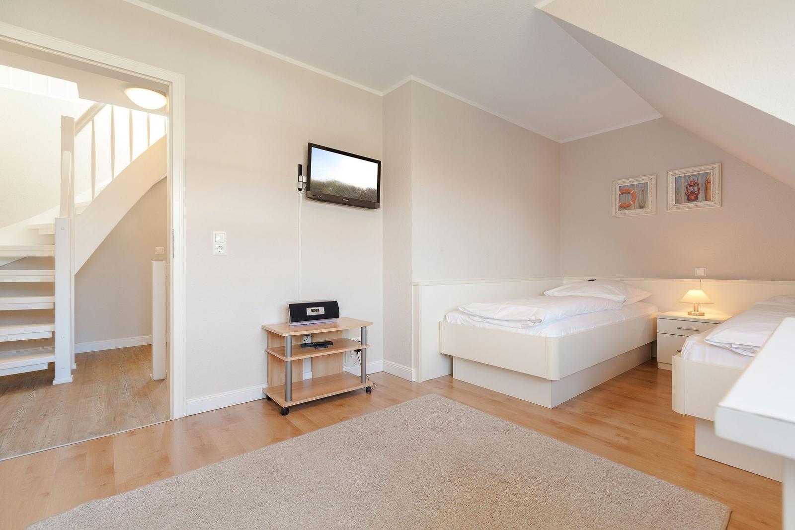Room with two beds, TV, and wooden floor