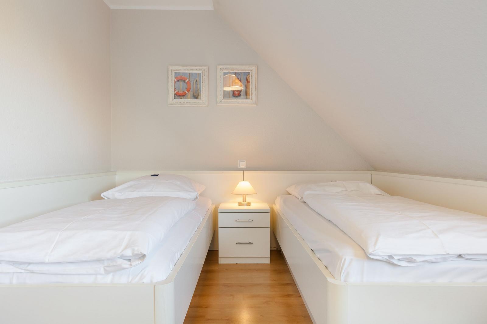 Two single beds with white bedding and nightstand under sloped ceiling