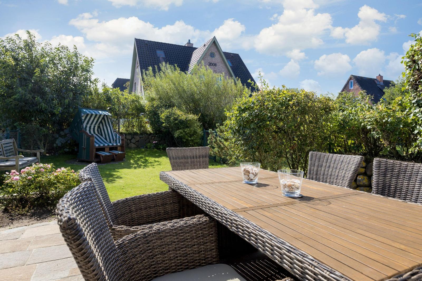 Deck with wooden table and chairs, lawn area and beach chair in background.