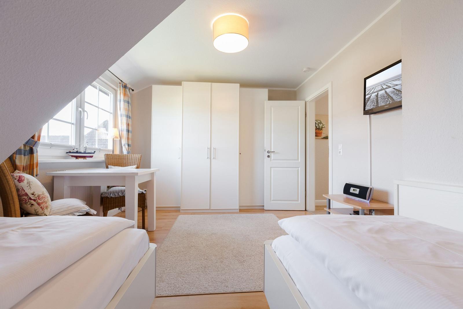 Room with two beds, desk, and wardrobe under sloped ceiling.