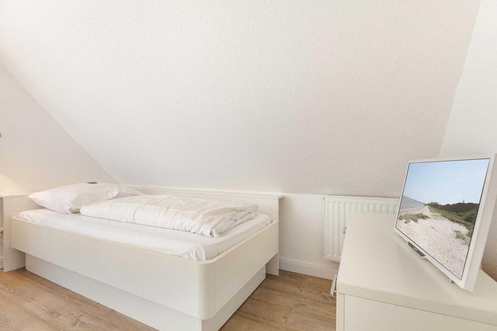 A bedroom with a white bed, wooden floor, and TV on a cabinet.