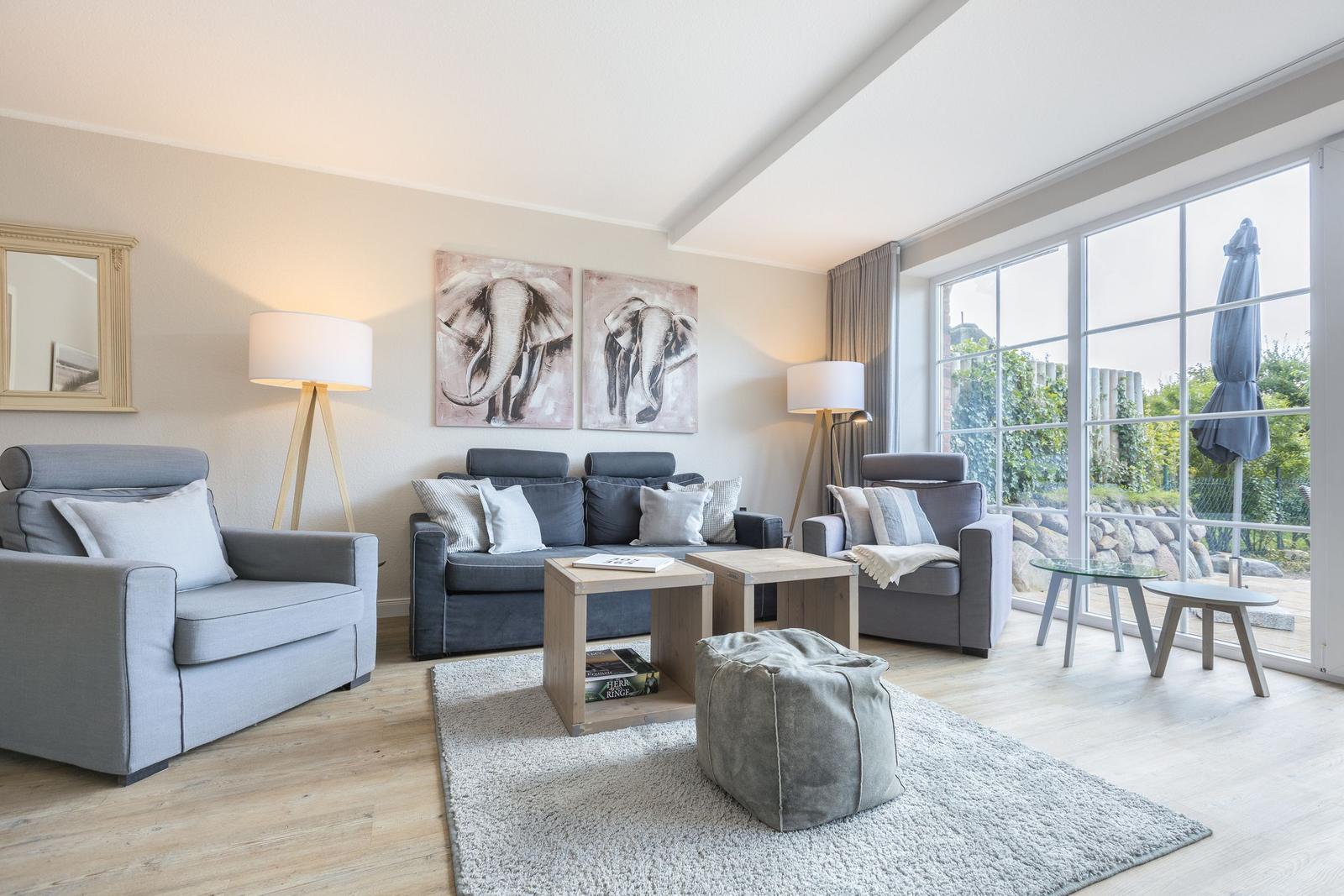 Living room with gray chairs, sofa, and cushions. Large window view to garden.