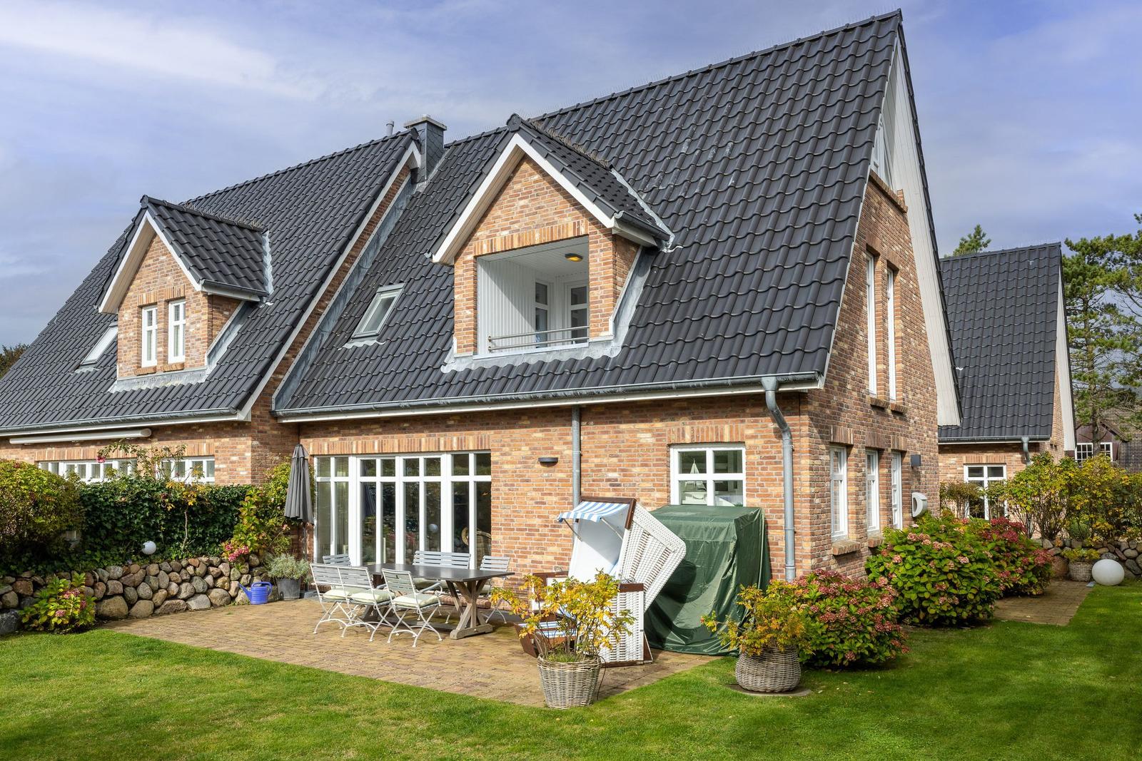 House with terrace, garden and wooden terrace. White windows and gray roof ridge.