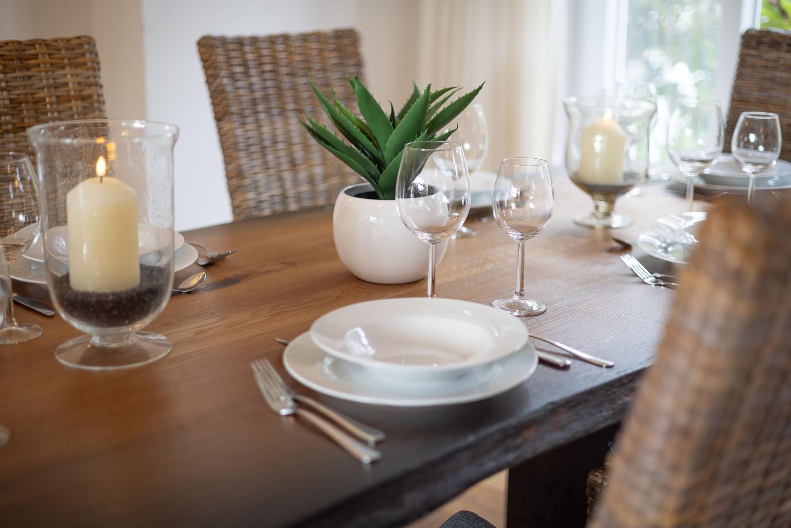 Wooden table with chairs, plates, glasses, and candles.