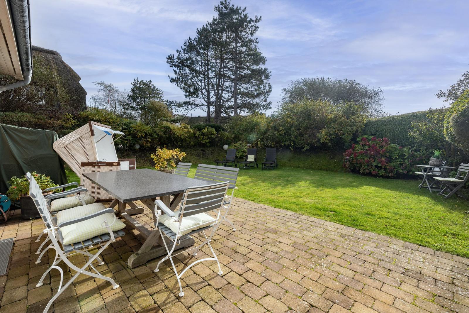 Terrace with table and chairs, green lawn and trees in the background.