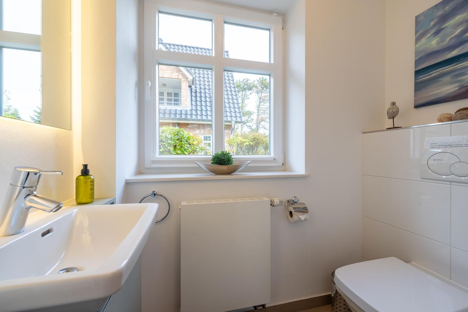Bathroom with sink, toilet, and window with view of house and trees.