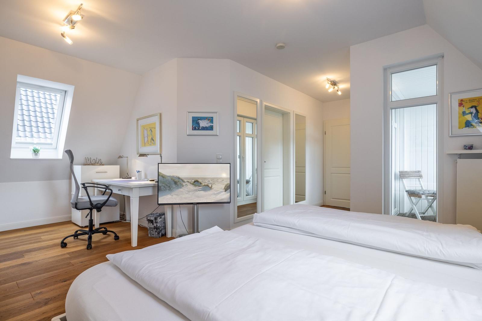 Bedroom with double bed, desk, and TV. Windows with view to balcony.