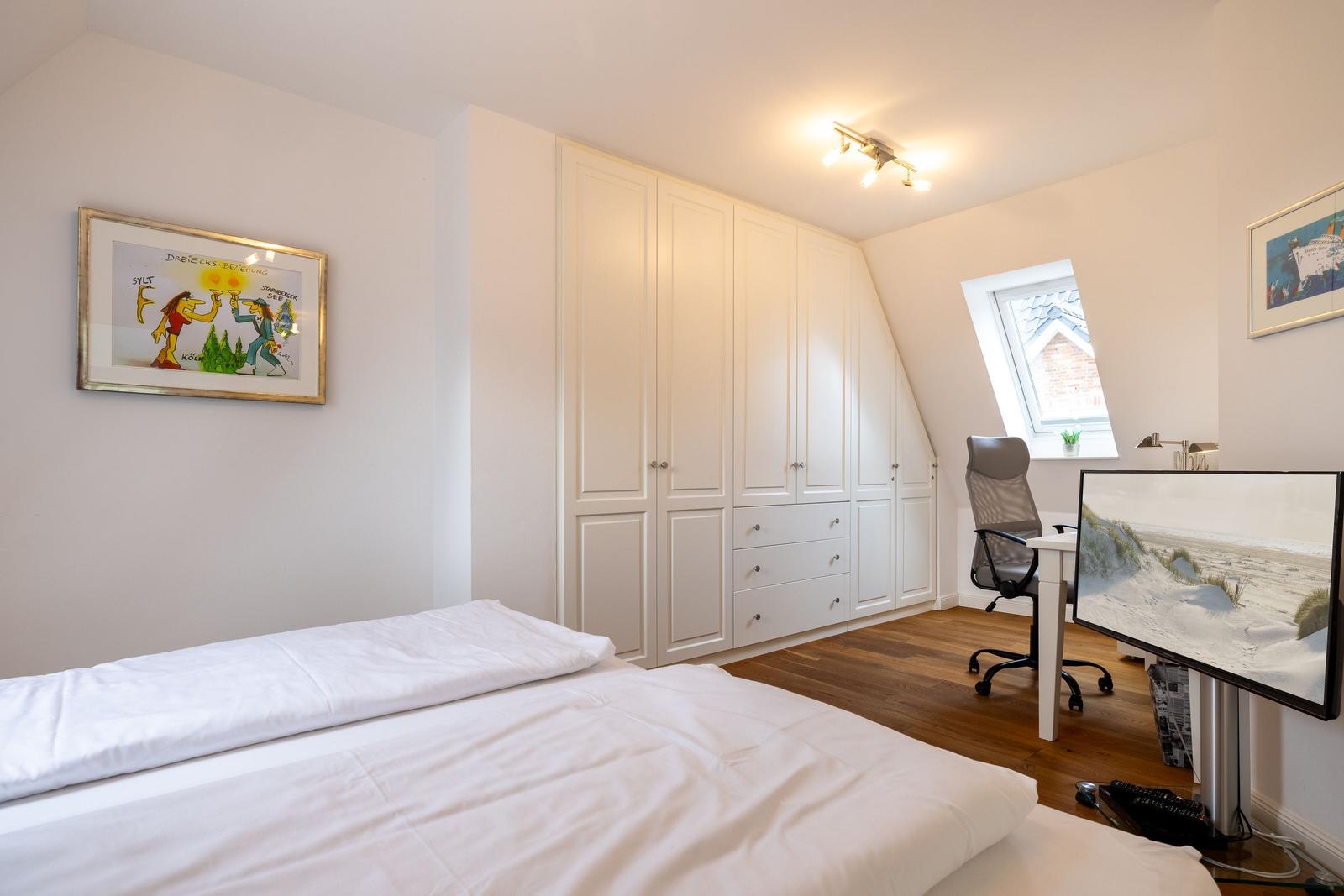 Bedroom with bed, wardrobe, and desk under sloped ceiling.