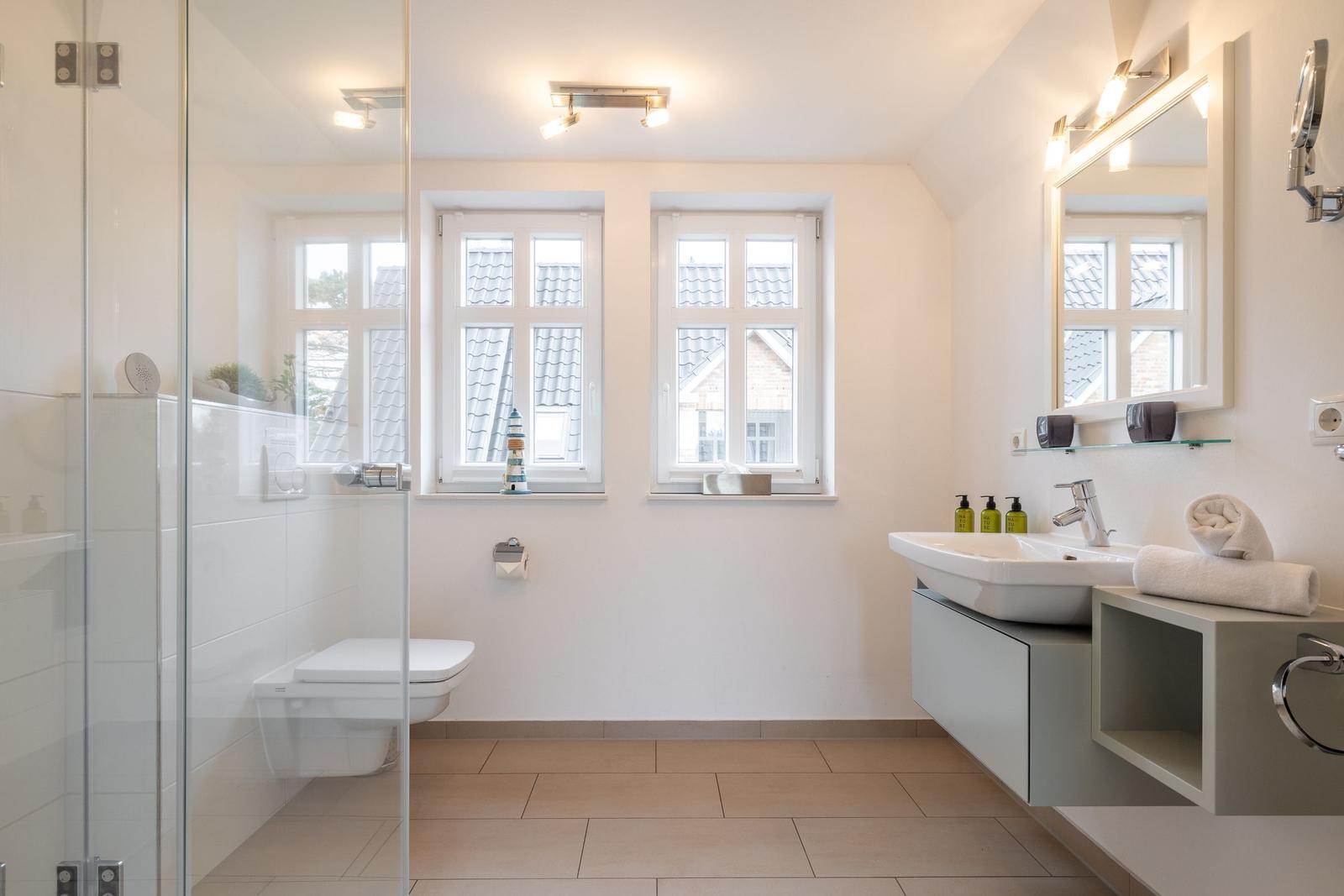 Bathroom with shower, toilet, sink, and windows.