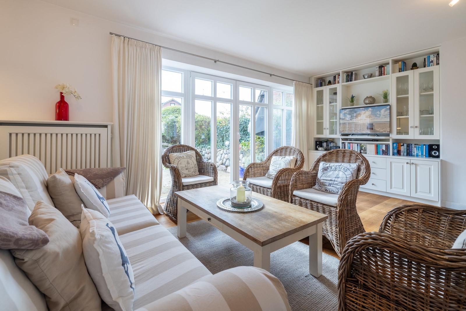 Living room with sofa, rattan chairs, and TV unit. Large windows with view outside.