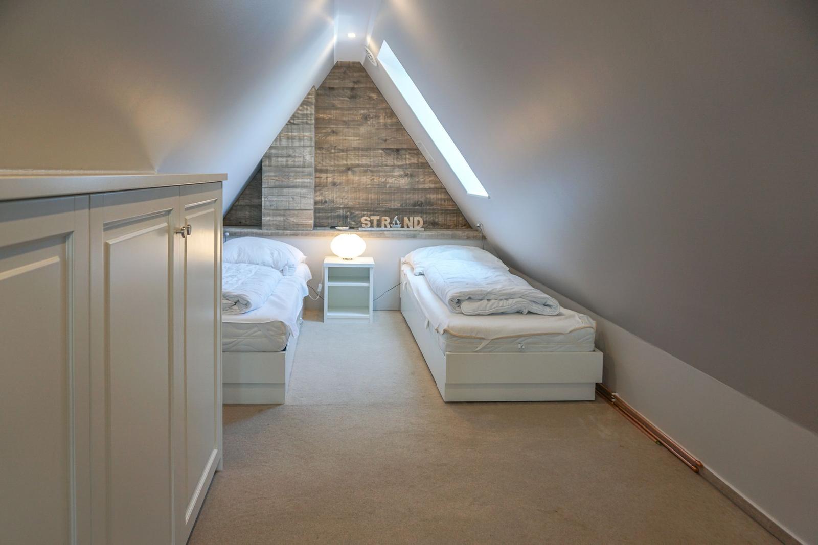 Two single beds in an attic room with wooden wall and skylight.