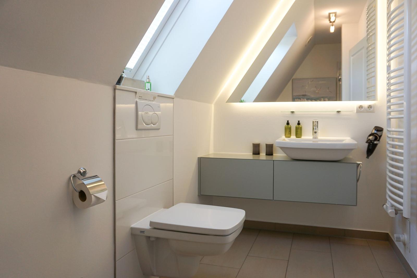 Bathroom with shower, sink and toilet under sloped ceiling.