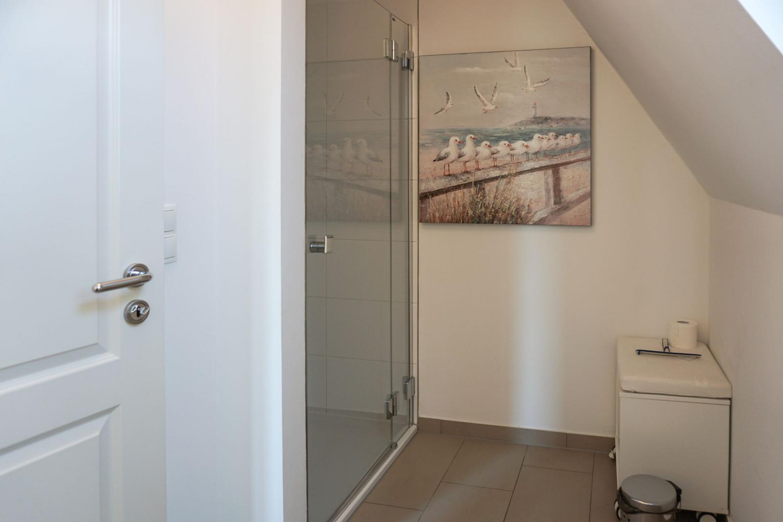 Shower area with glass enclosure, seagull artwork, and toilet cabinet.