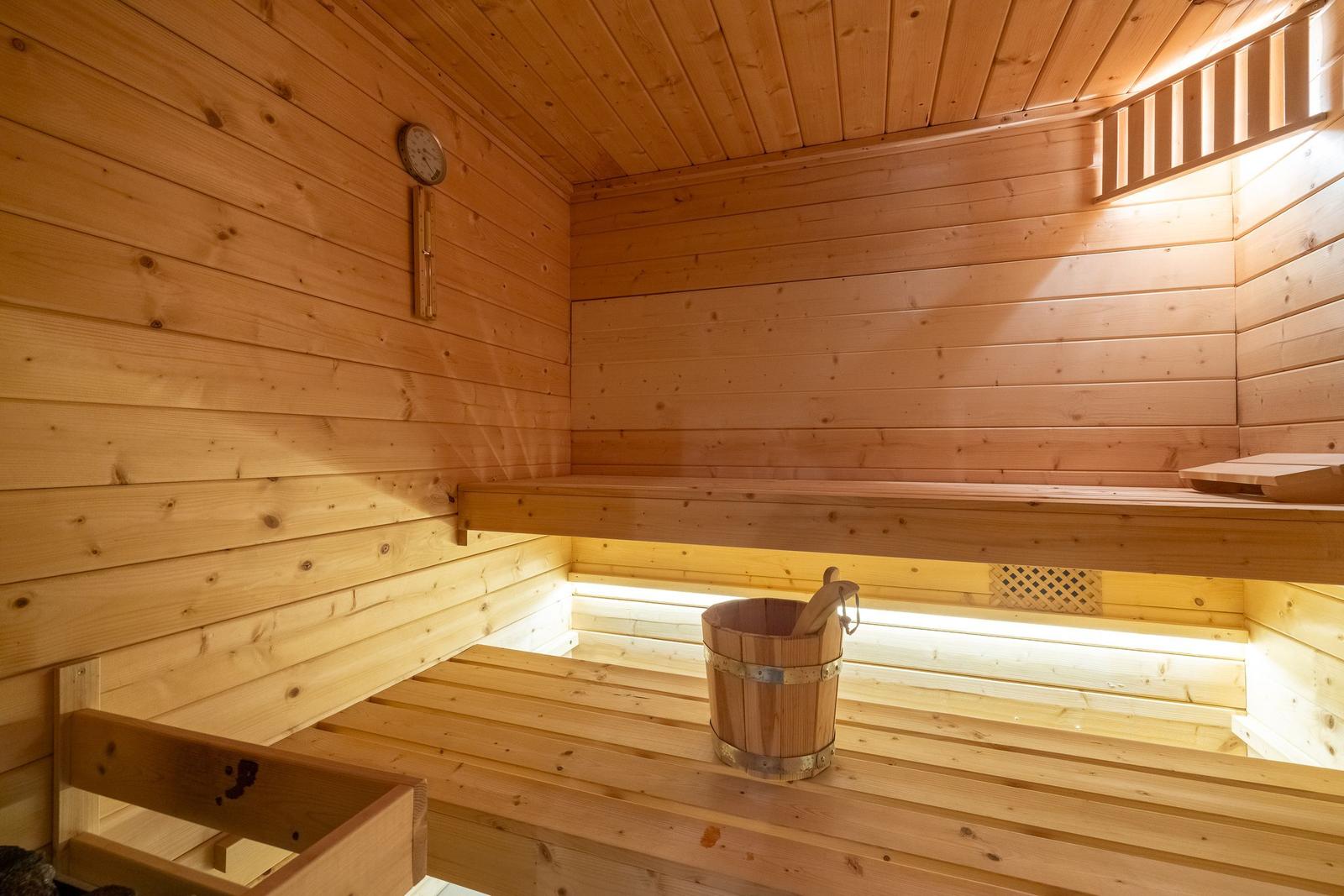 Sauna with wooden bench, bucket, and thermometer on the wall.