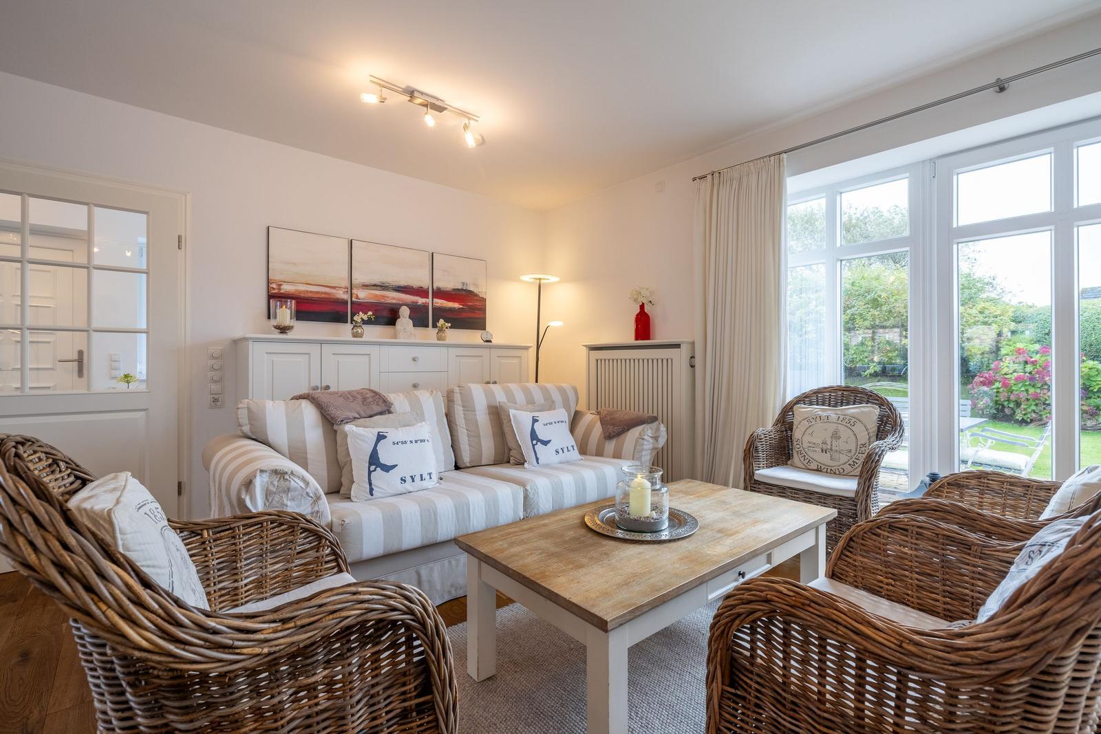 Living room with sofa, wicker chairs, and large window to the garden.