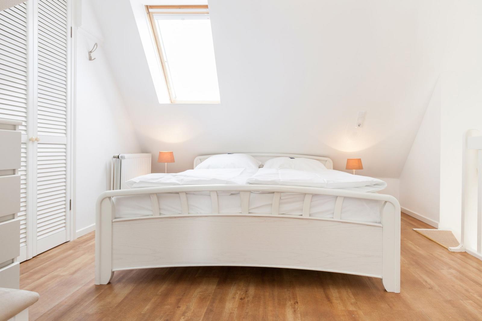 Schlafzimmer mit Dachfenster, weißem Bett und Holzboden.