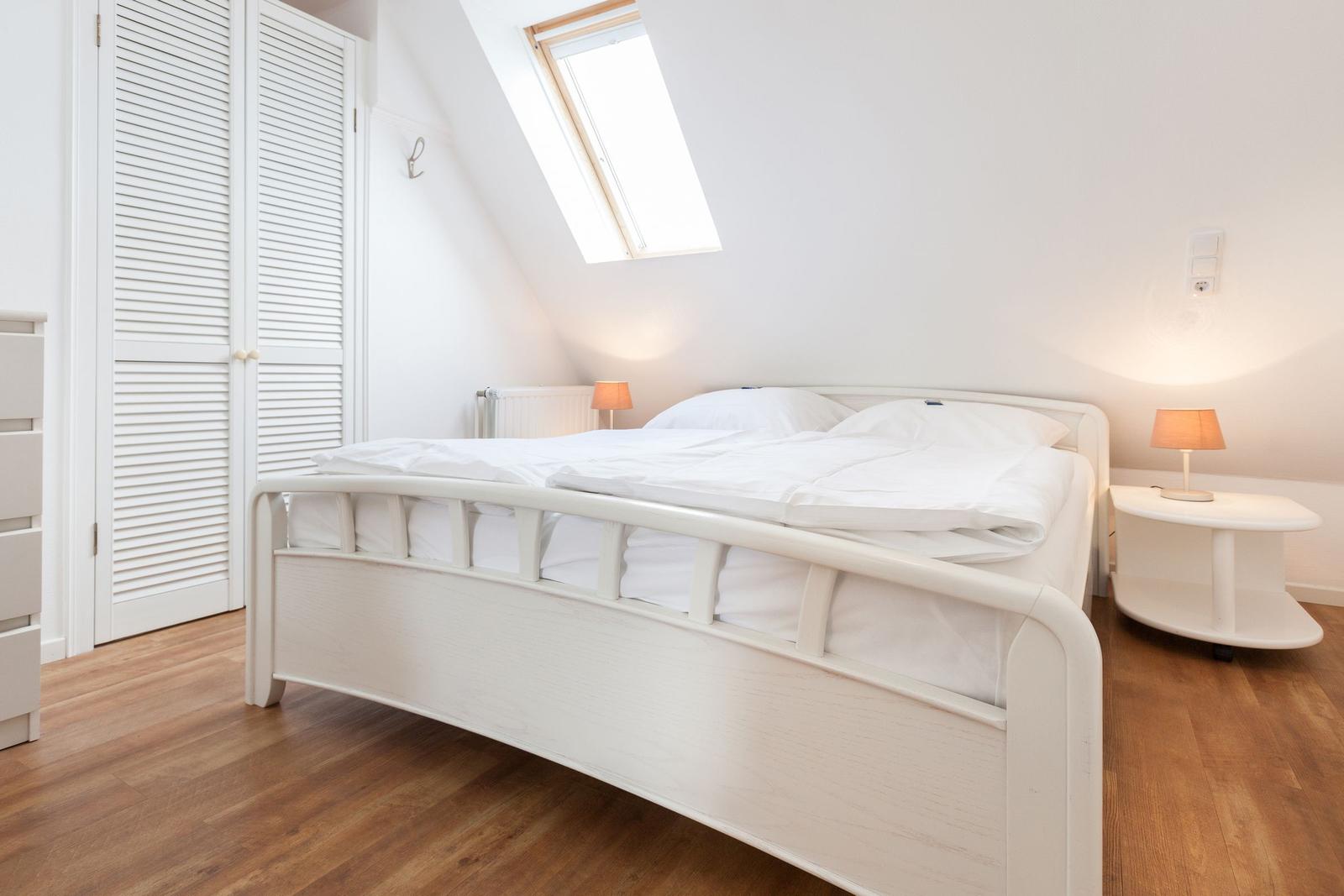 Schlafzimmer mit Dachschräge, weißem Bett und Holzboden