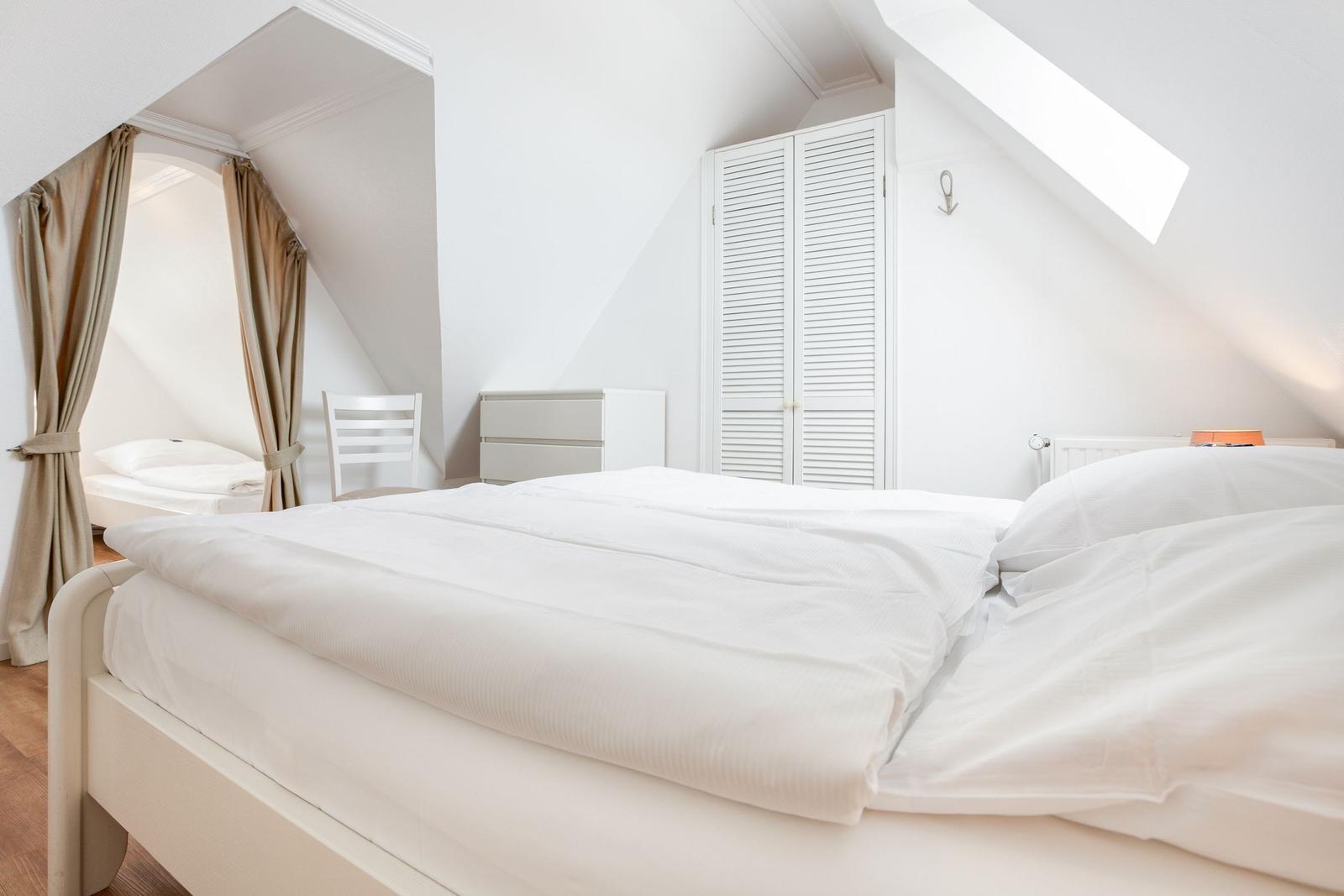Schlafzimmer mit Dachschrägen, Doppelbett und kleinem Bett.