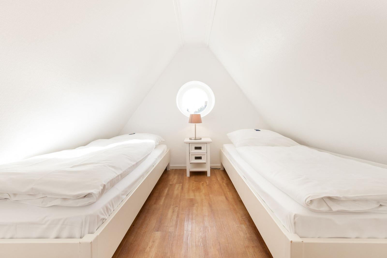 Zwei Betten in einem Dachzimmer mit runden Fenster und Nachttisch.