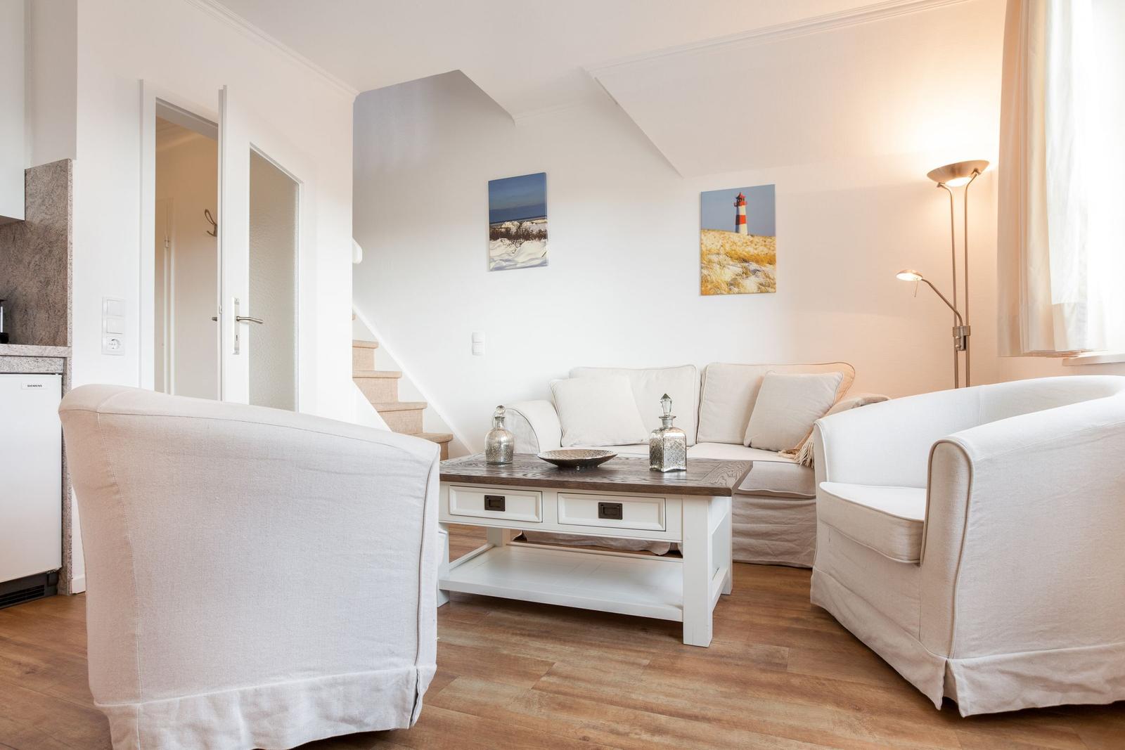 Wohnzimmer mit Sofa, zwei Sesseln und Holzboden. An der Wand hängen zwei Bilder.