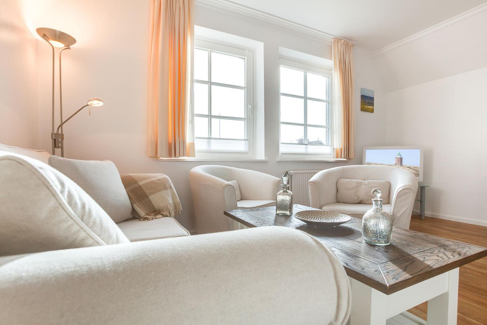 Wohnzimmer mit Sofa, zwei Sesseln, Tisch und Fenstern.