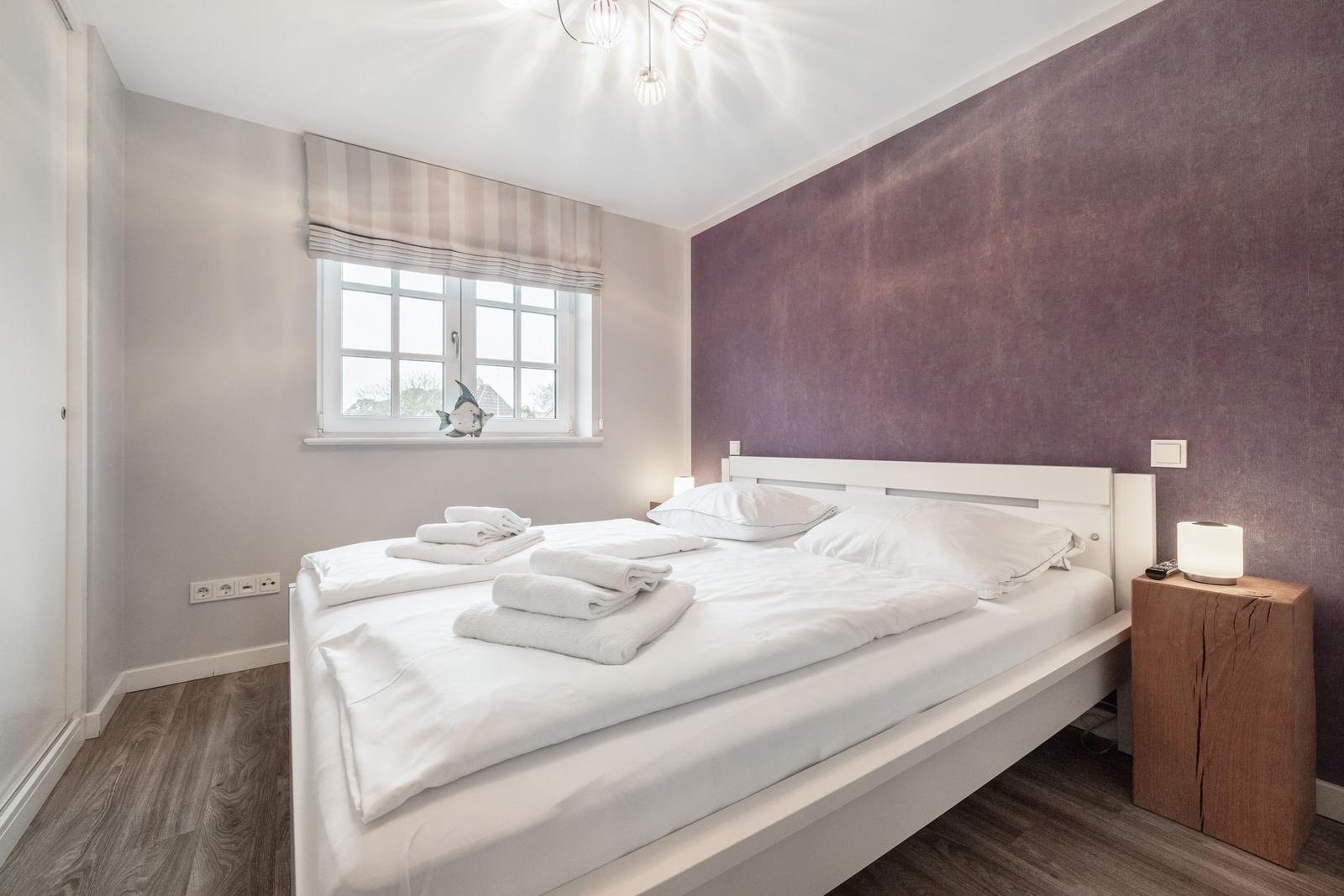 Bedroom with white bed, purple wall, and wooden side table.