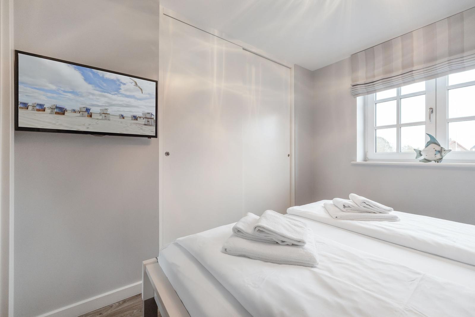 Bedroom with bed, window, and wall picture. White bedding and towels.